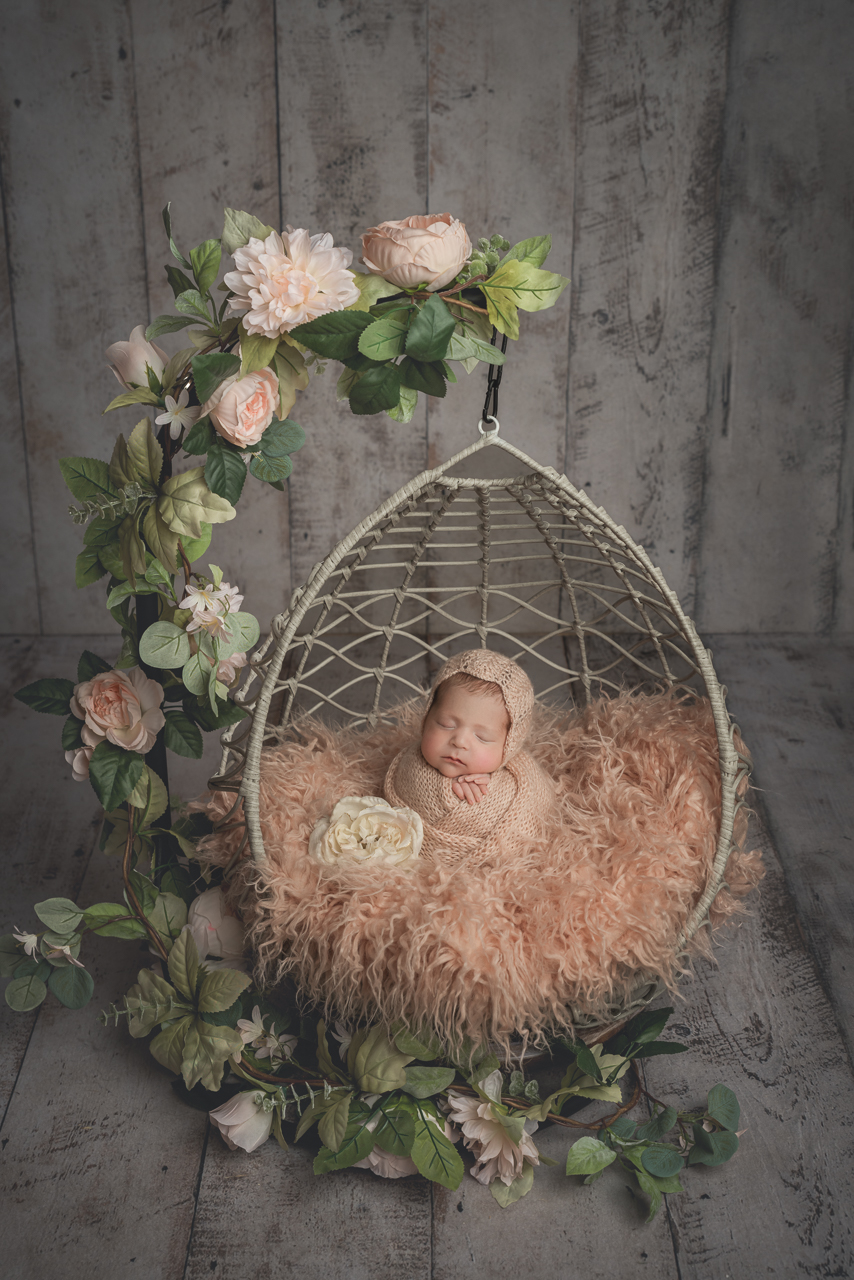 Newborn in pink fuzzy wrap posed in floral hanging swing during styled newborn photography session in North Ogden
