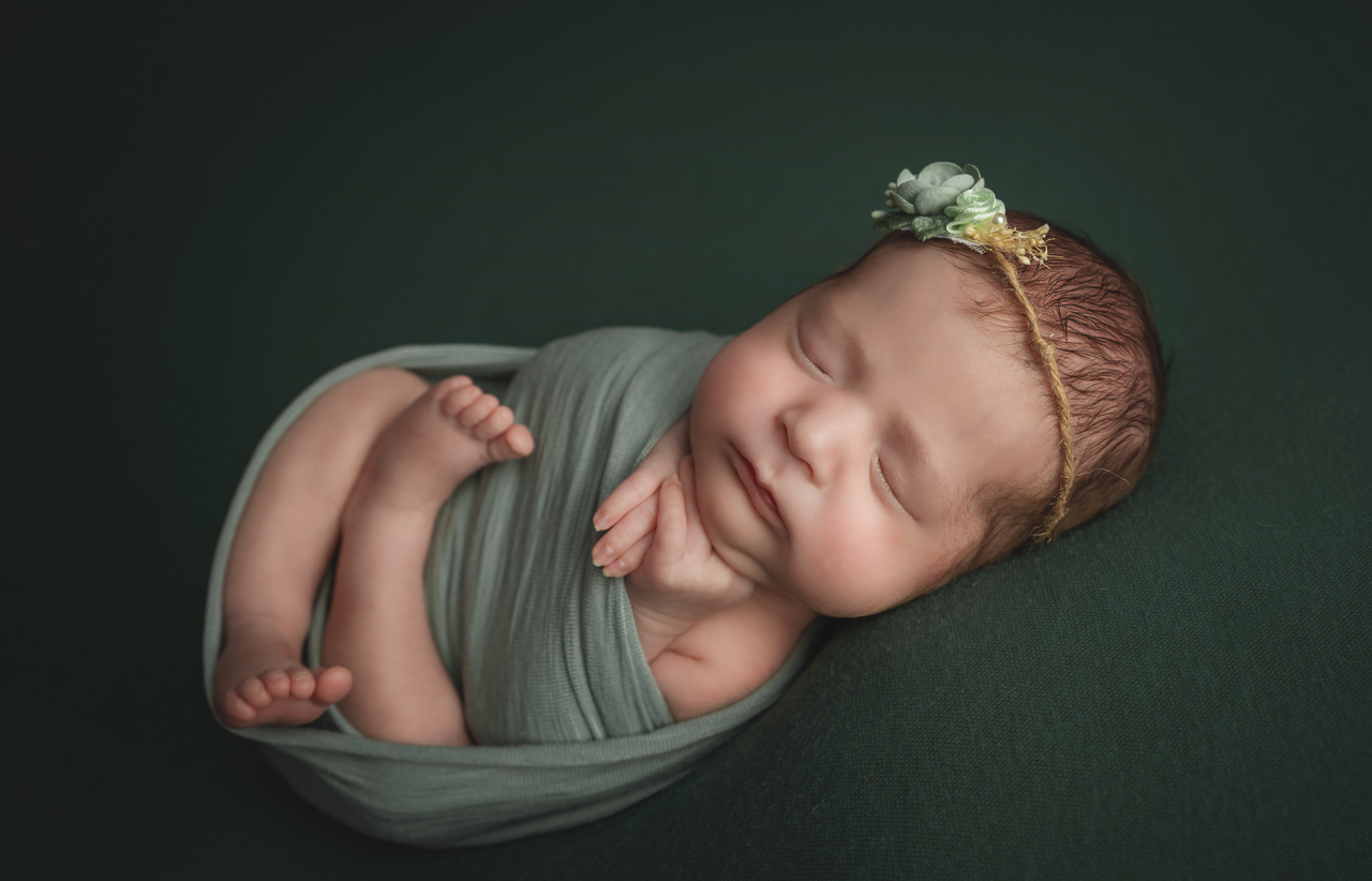 Newborn girl in wrap and headband egg pose