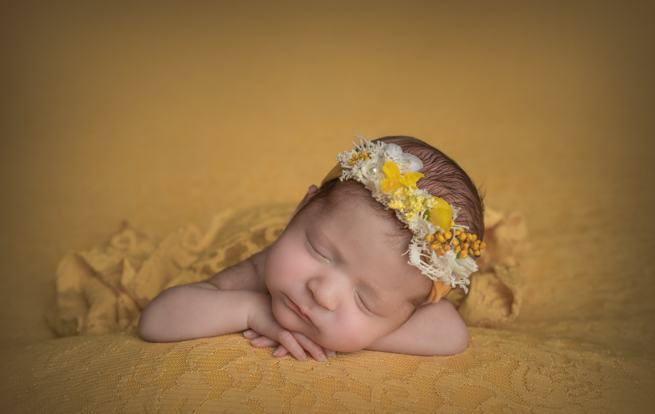 Newborn baby girl posed on yellow lace blanket wearing yellow floral headband at Ogden Utah newborn session