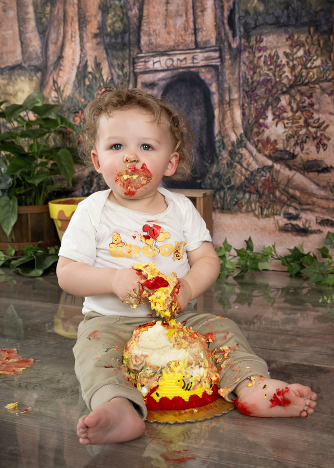 Smash cake photo with baby enjoying Winnie the Pooh-themed birthday cake in custom set design
