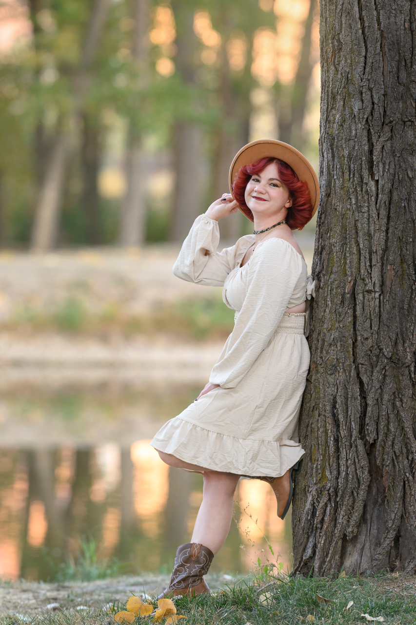 DS1_5231 Red-haired teen girl in cream dress and hat smiling near a pond in fall for family photography in North Ogden