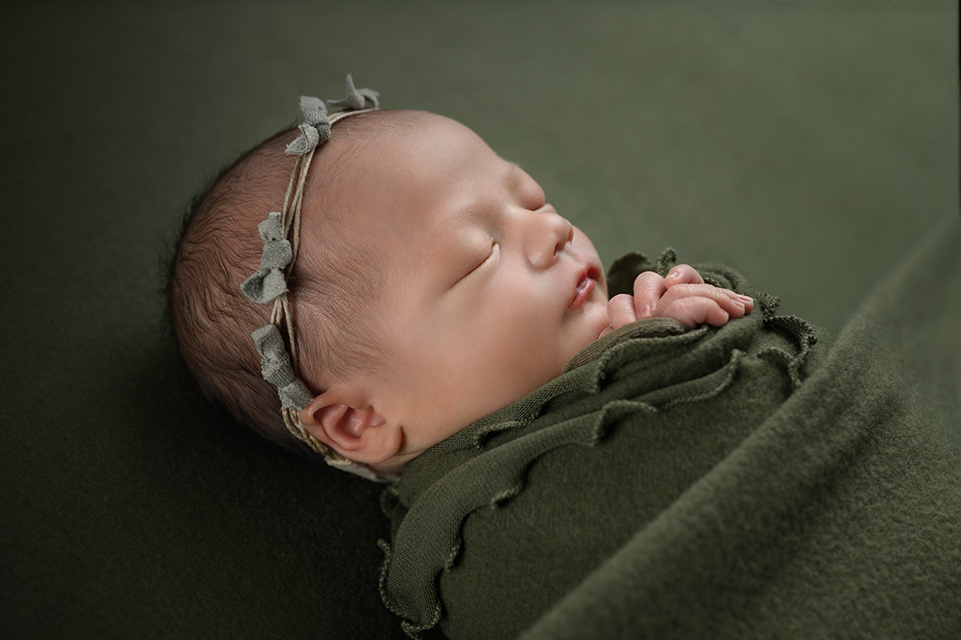 Newborn girl with headband on green all wrapped up and sleeping in north ogden photo studio