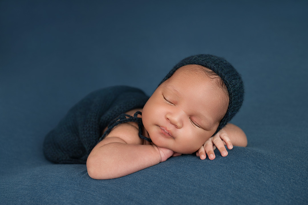 newborn baby photography on blue in chin on hands with bonnet